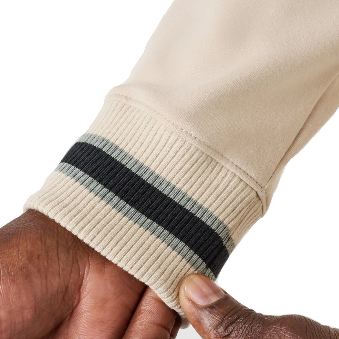 Close-up of a beige sweatshirt sleeve with a black and gray striped cuff on a neutral background.
