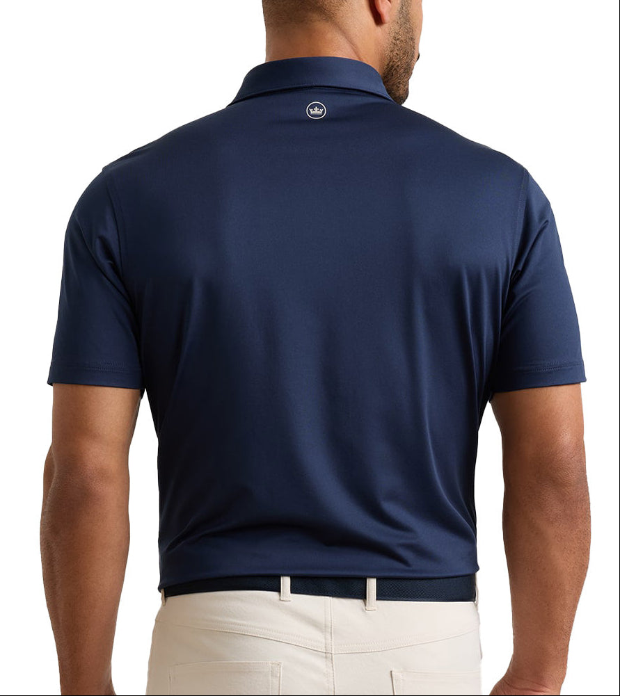 A man viewed from the back wearing a navy blue short-sleeve polo shirt and light beige trousers, shown against a plain white studio background.