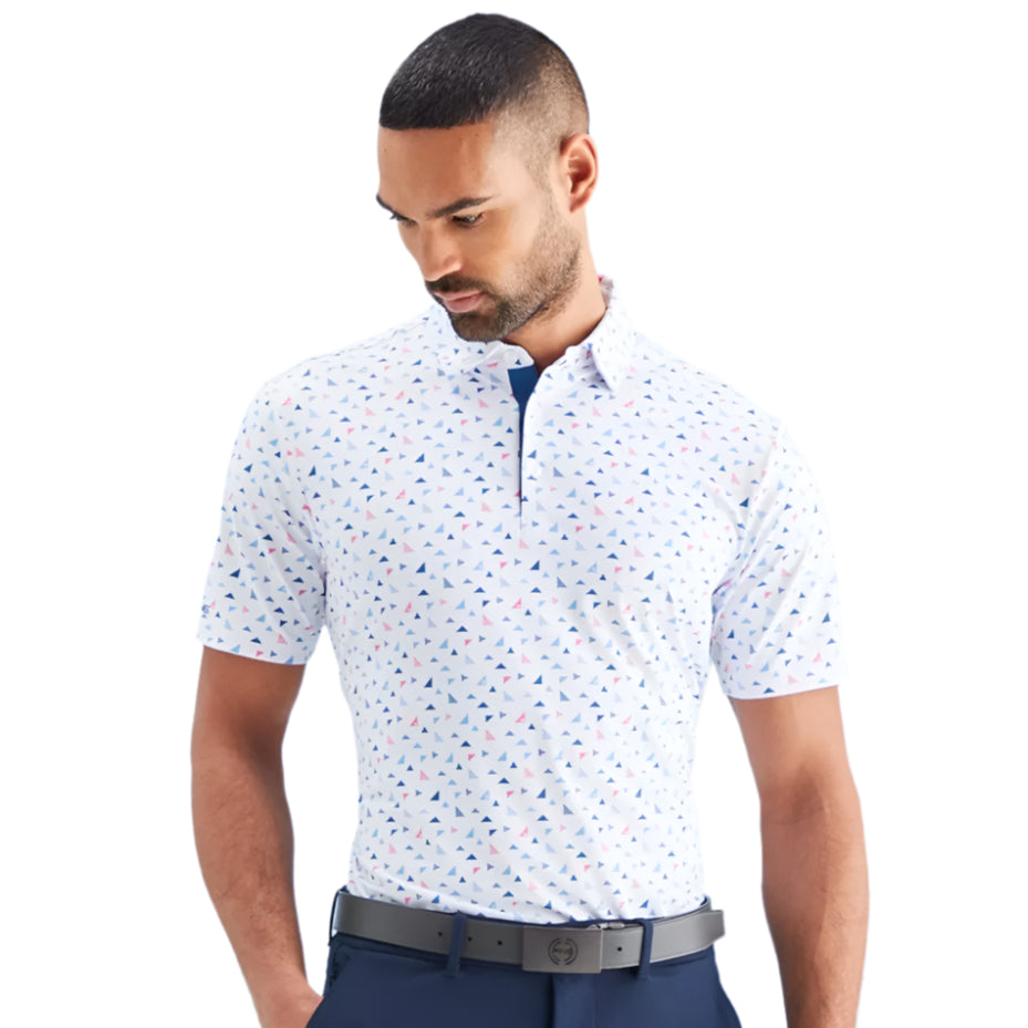 Man wearing a patterned short-sleeve shirt and navy pants against a light blue background