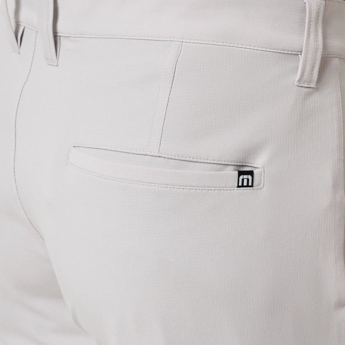 Close-up of light gray pants with a brand logo on the pocket.