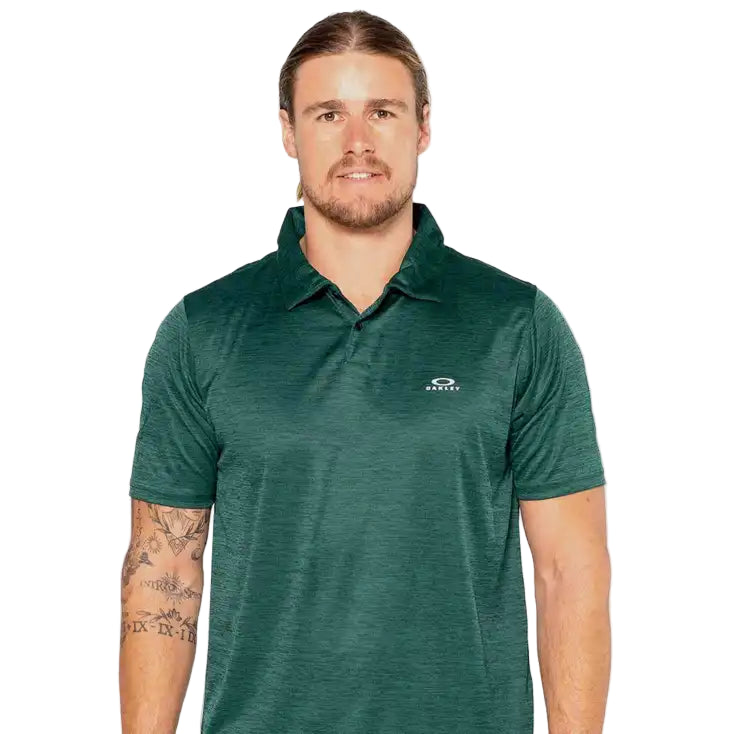 Man wearing a green polo shirt with a logo on a light gray background