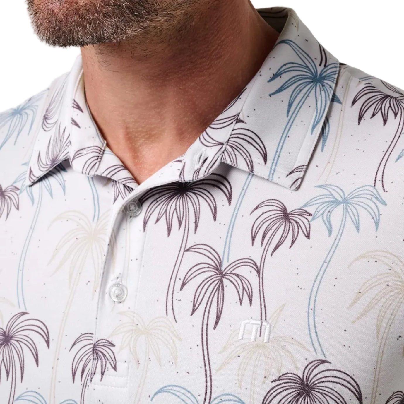 Close-up of a white polo shirt with palm tree pattern worn by a person.