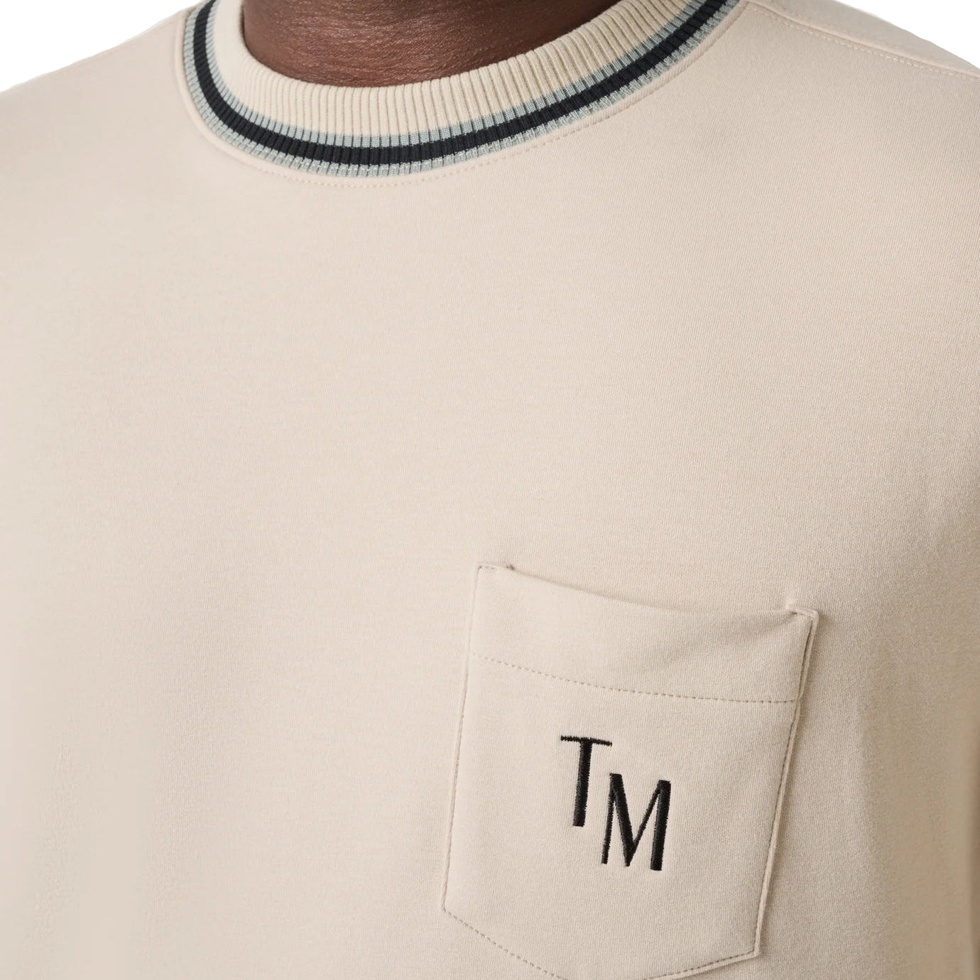 Beige sweater with a pocket and 'TM' monogram on a plain background