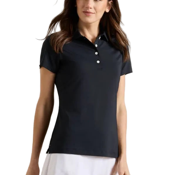 A woman modeling a short-sleeve polo shirt in dark navy blue paired with a white skirt, photographed against a plain light beige studio background.