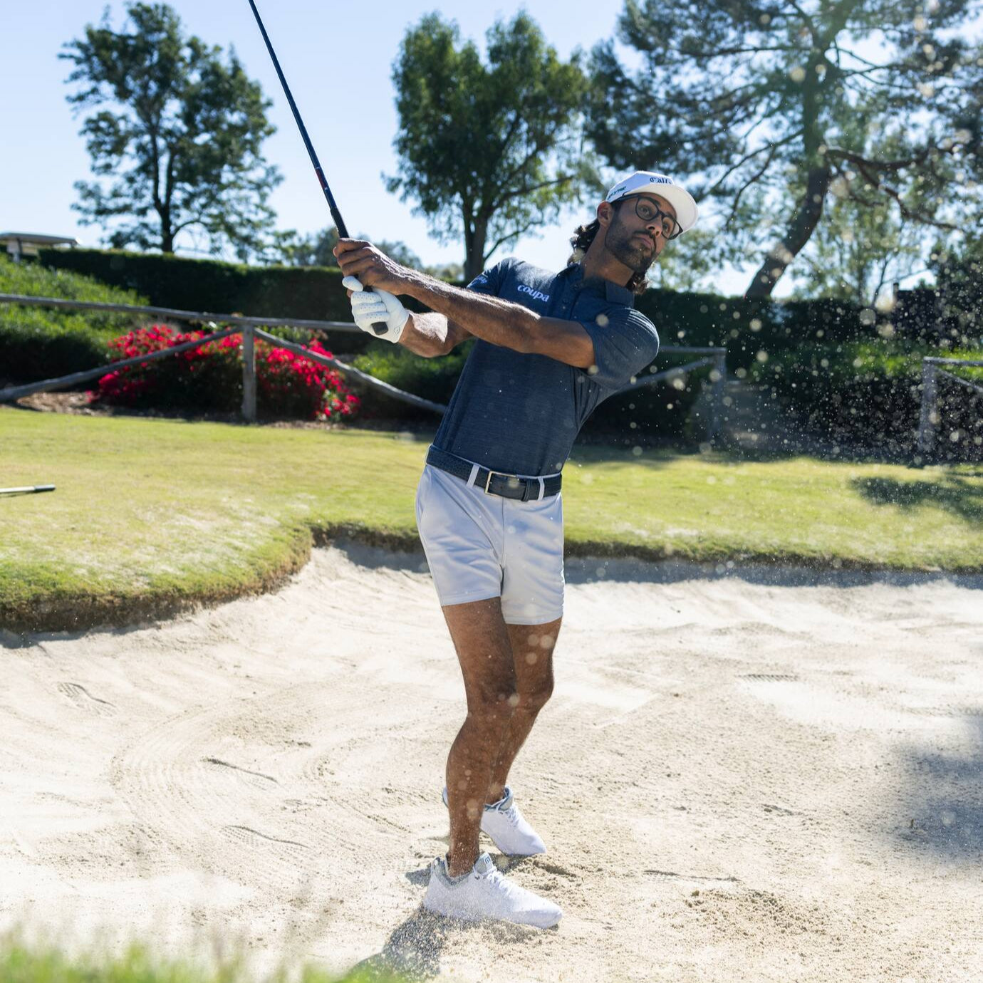 Golfer in a sand trap on a golf course with trees and flowers in the background