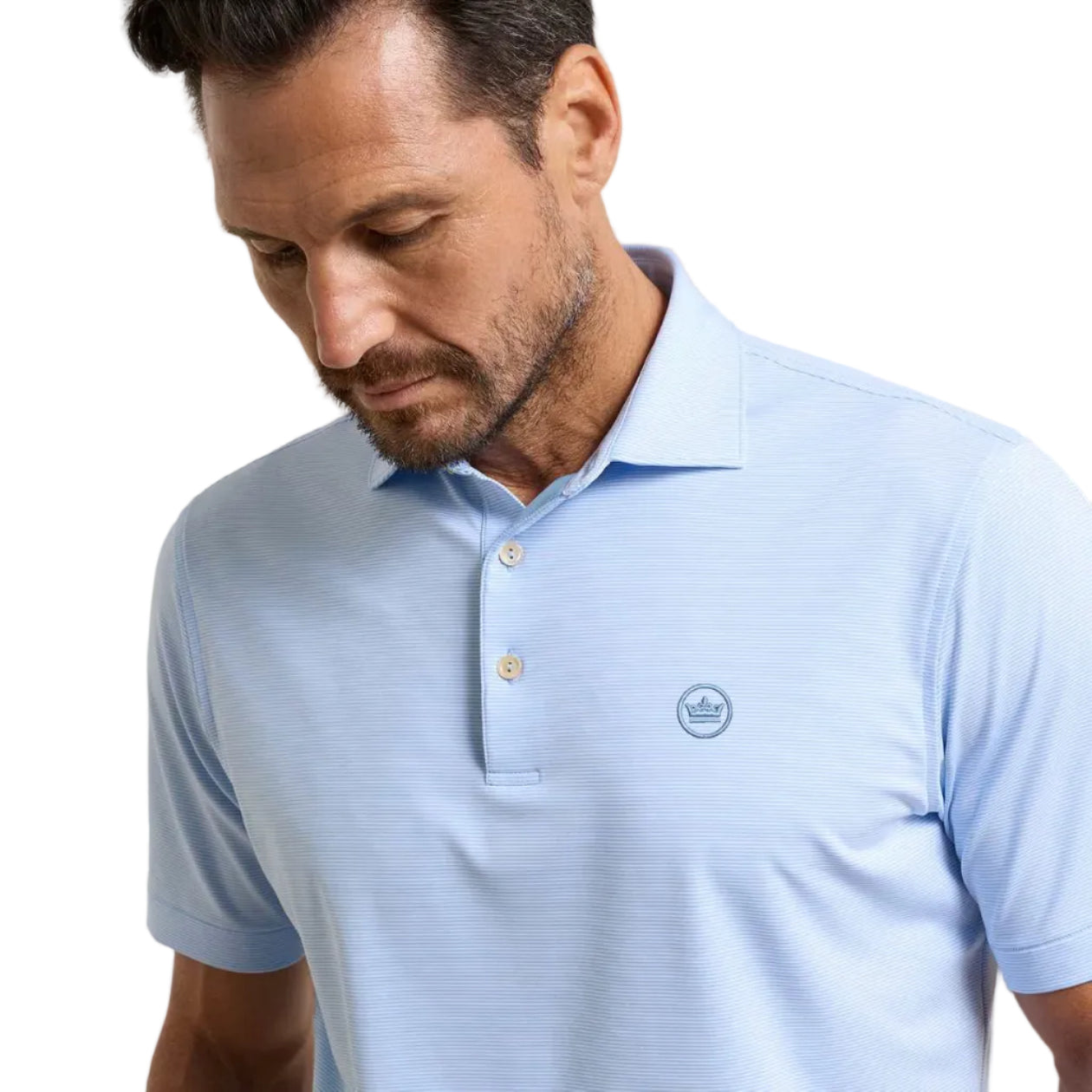 A man wearing a light blue short-sleeve polo shirt with a small circular embroidered logo on the left chest, photographed against a soft beige studio background.
