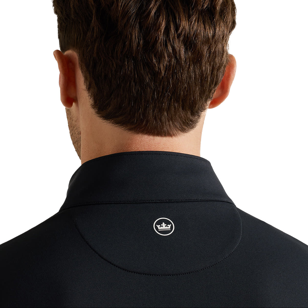 Back view of a man wearing a black high-collar pullover top, showing a small white crown logo on the back of the neck, against a plain white background.