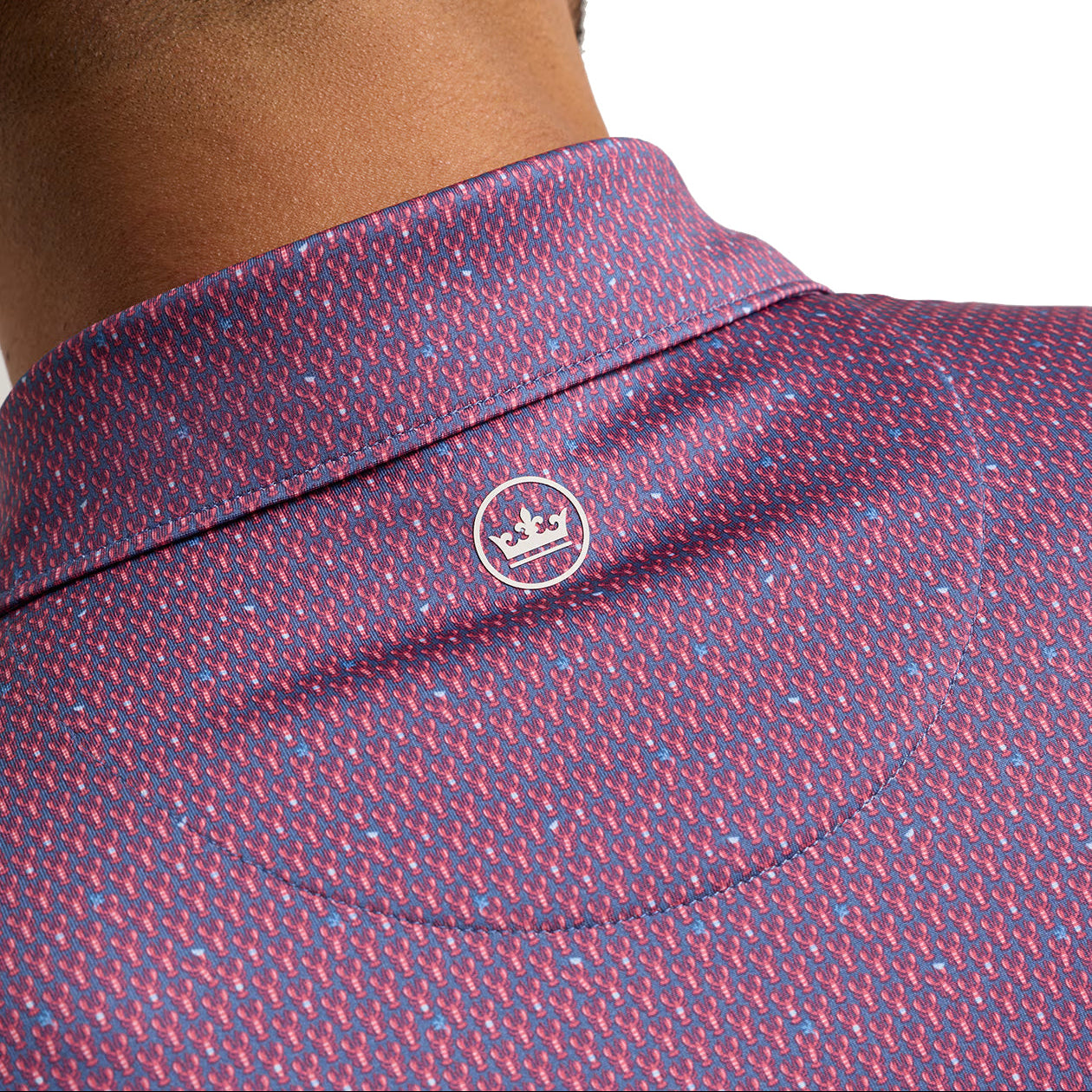 Close-up of the back of a man's neck and upper shoulder wearing a collared shirt with a dense micro-pattern in red, blue, and white, featuring a small circular embroidered logo on the collar.