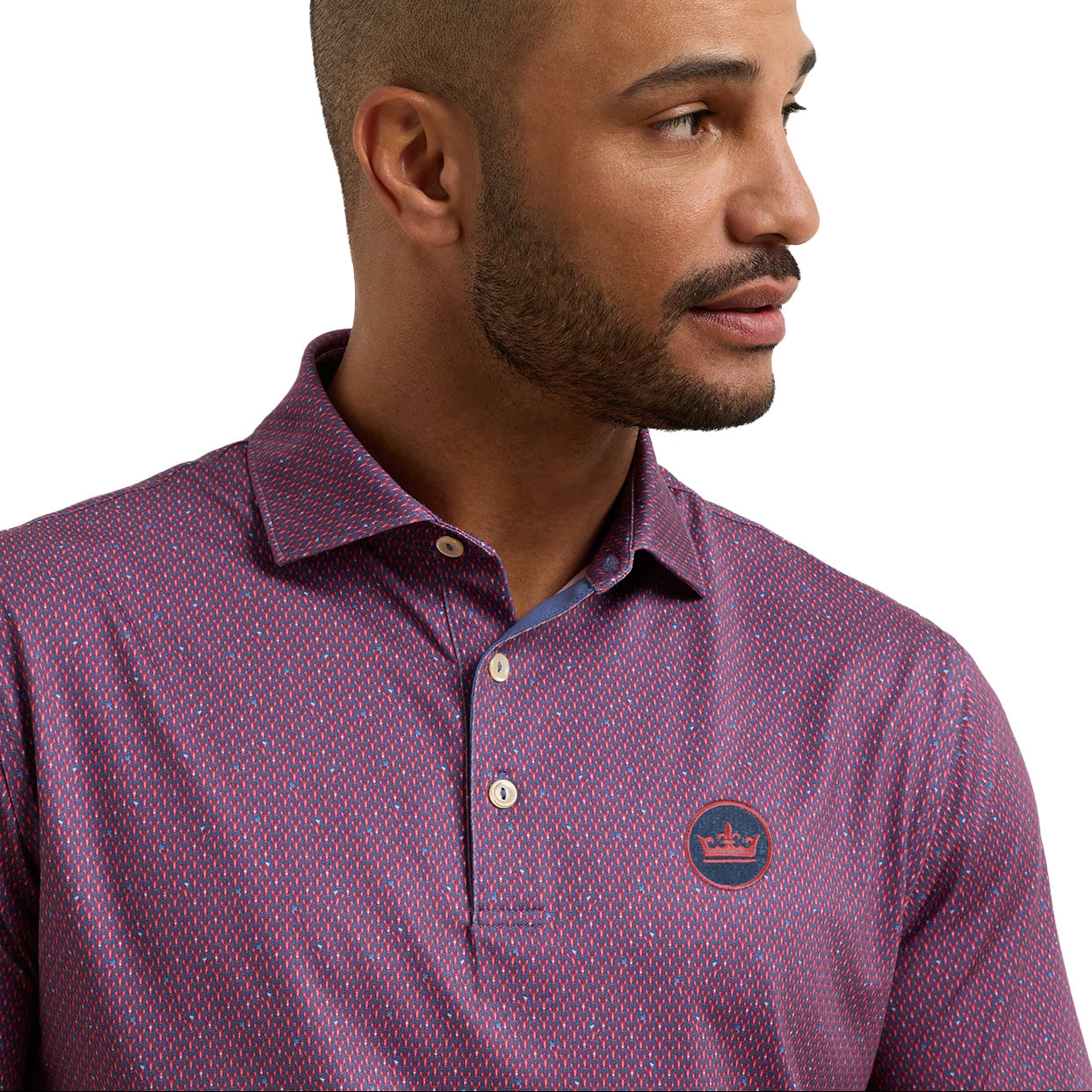 A close-up of a man wearing a short-sleeve polo shirt with a purple and red micro-pattern, featuring a small circular logo patch on the left chest.