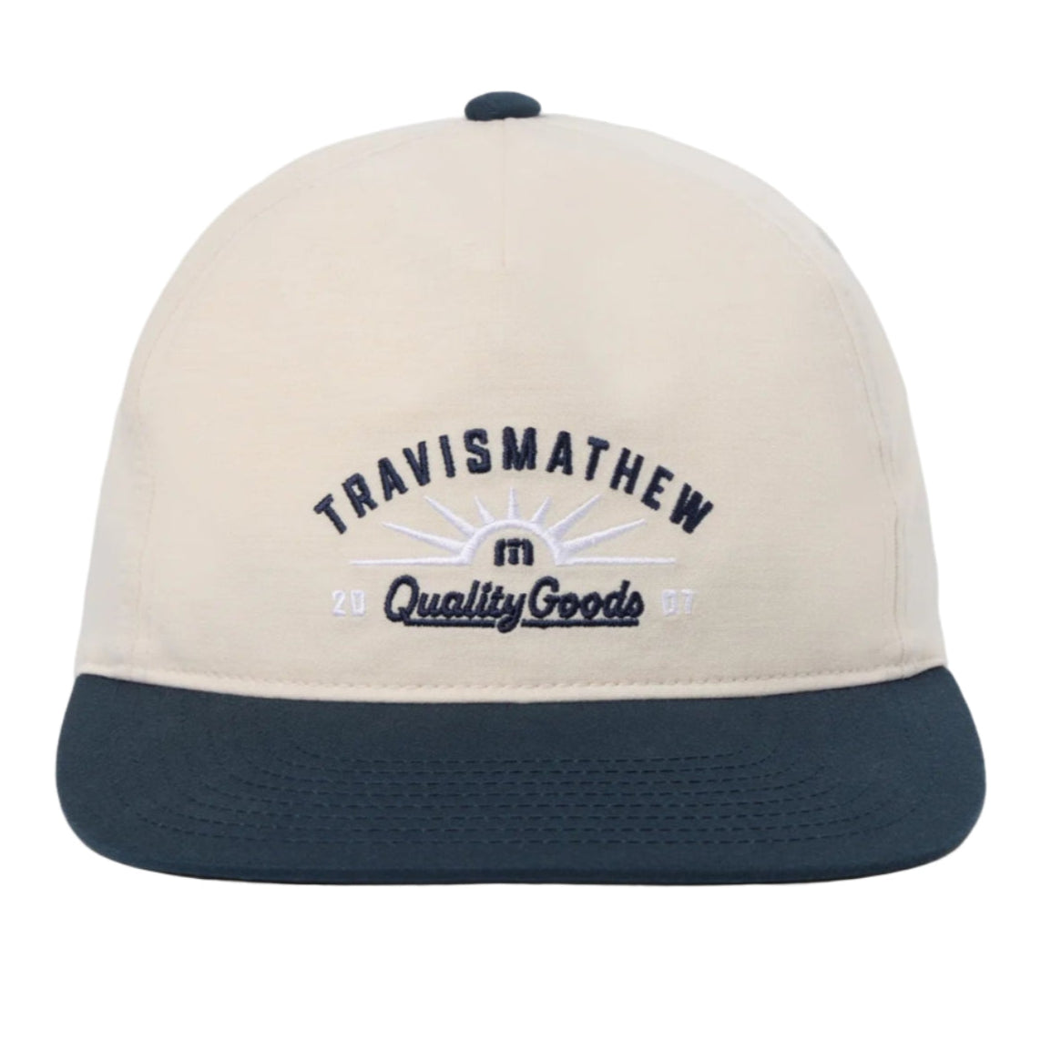 Beige and navy cap with 'TravisMathew Quality Goods' logo on a white background